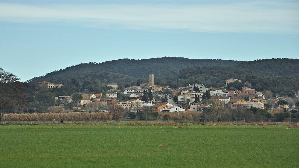 Une ville avec un imposant clocher d’église qui domine une colline, entourée de bâtiments résidentiels et d’un champ verdoyant au premier plan.