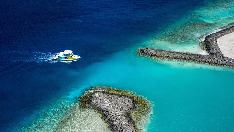 A boat on turquoise waters, a rocky shoreline, and a sandy beach.