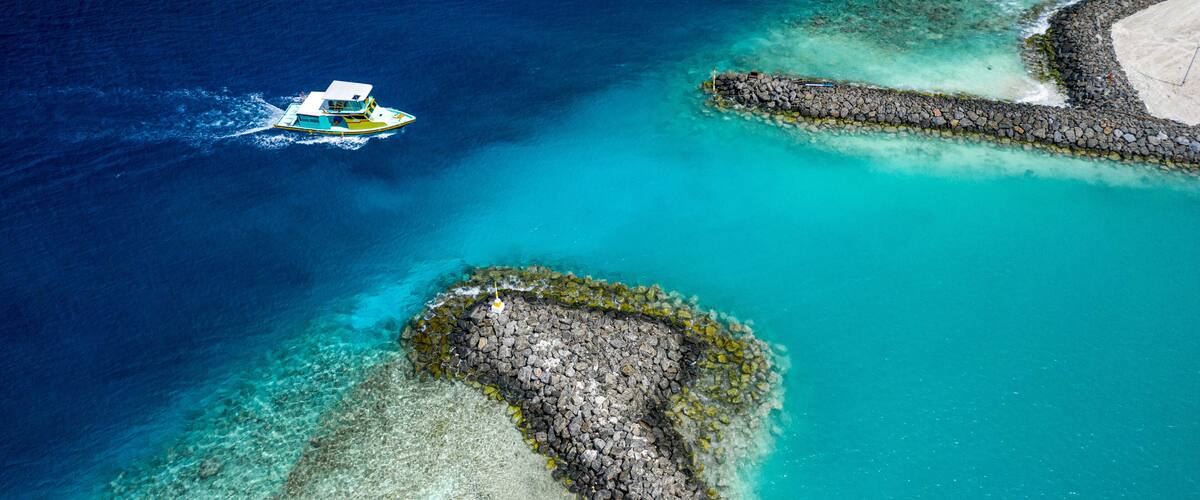 A boat on turquoise waters, a rocky shoreline, and a sandy beach.