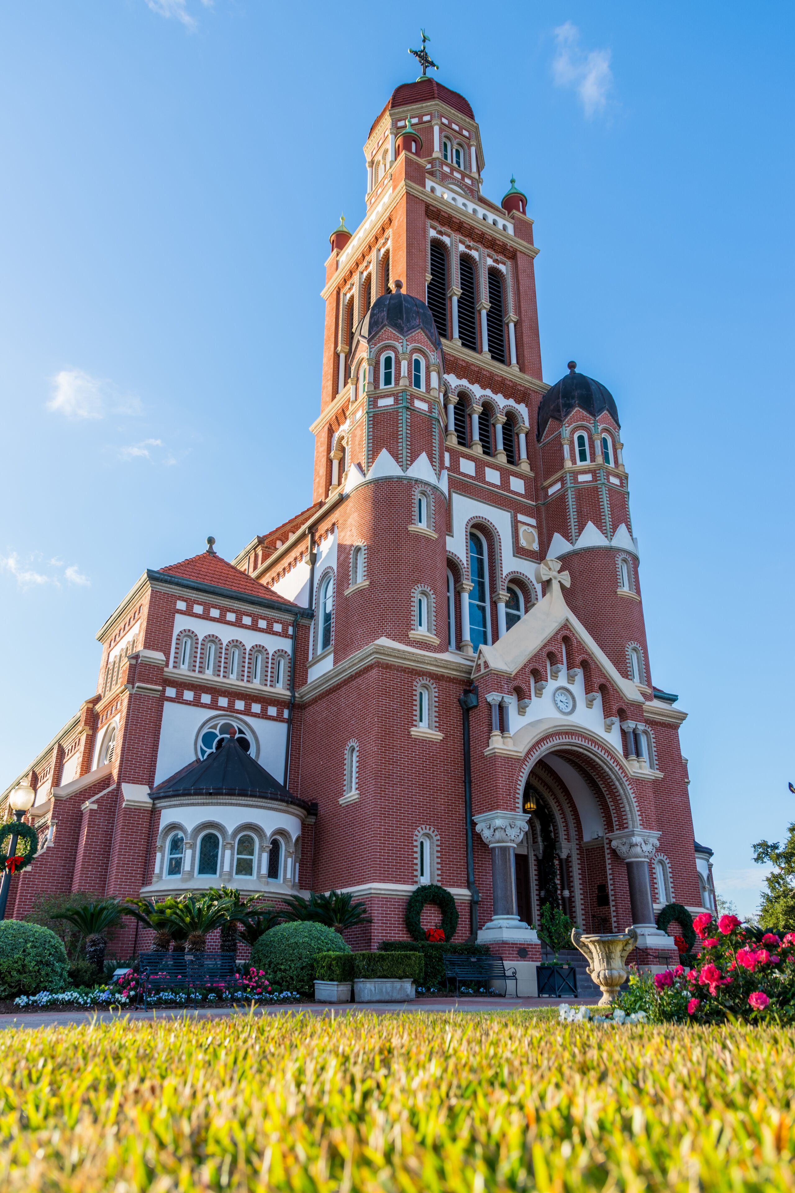 A large red brick church with a bell tower, surrounded by a well-maintained garden with flowers and a lawn.