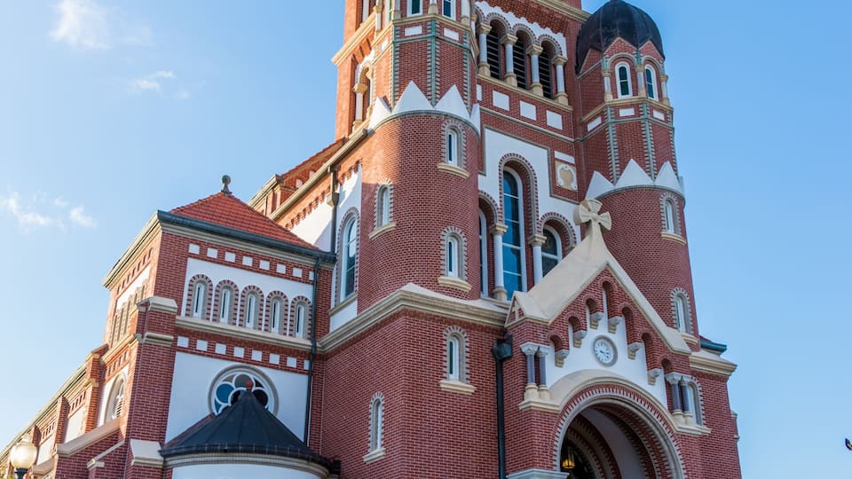 A large red brick church with a bell tower, surrounded by a well-maintained garden with flowers and a lawn.