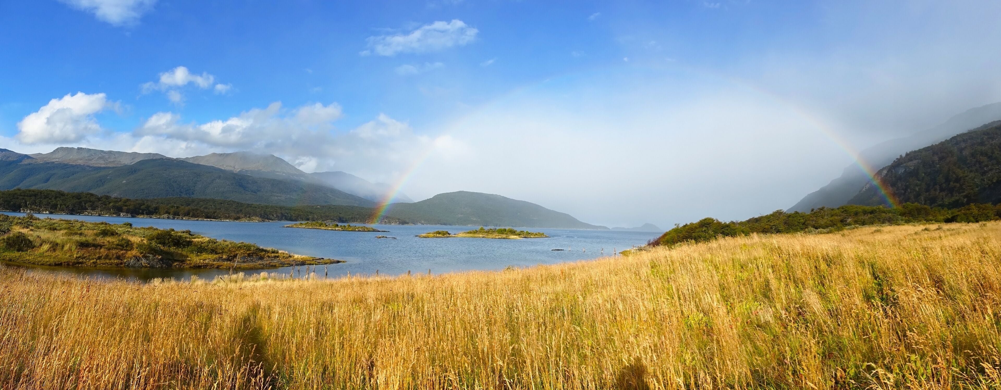A lake with islands, mountains, and a rainbow.