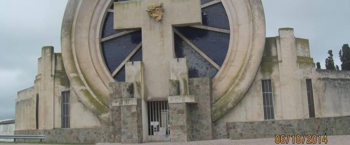 A large circular building with a cross in the center, surrounded by stone walls and a gate.