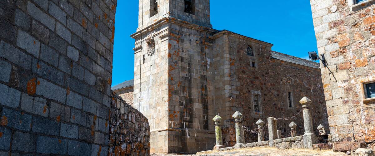 A historic stone building with a bell tower, surrounded by other stone structures.