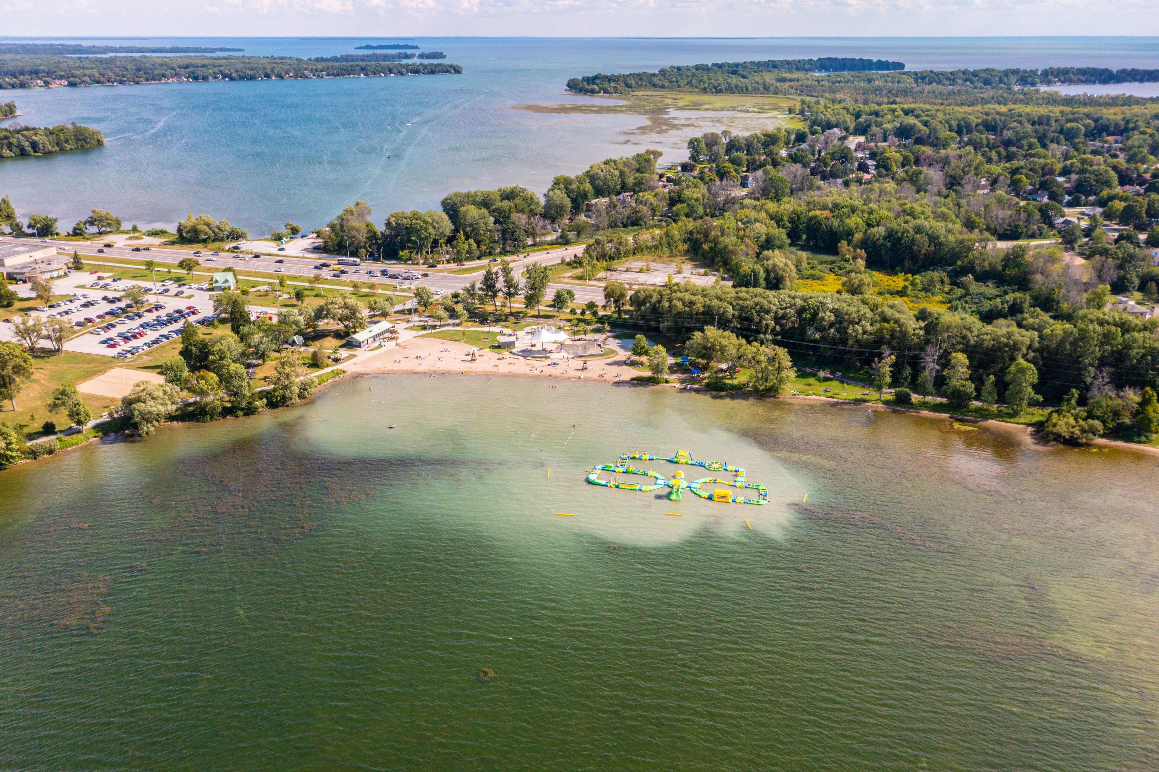 A lake with a boat-shaped island, a parking lot, and a residential area with houses and trees.