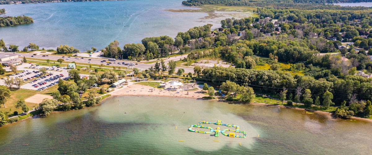 A lake with a boat-shaped island, a parking lot, and a residential area with houses and trees.