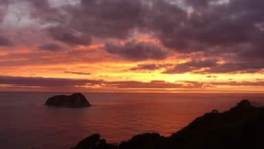 Un atardecer sobre un mar tranquilo con una pequeña isla en primer plano y un cielo nublado.