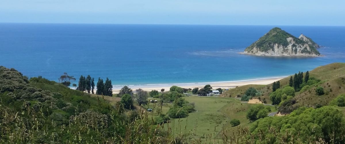 A coastal landscape with a small island, a beach, and rolling hills.