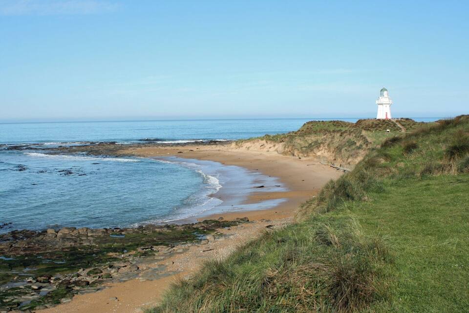 A coastal landscape with a lighthouse on a grassy cliff overlooking the sea.