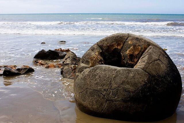 Uma grande formação rochosa numa praia, com o oceano ao fundo.