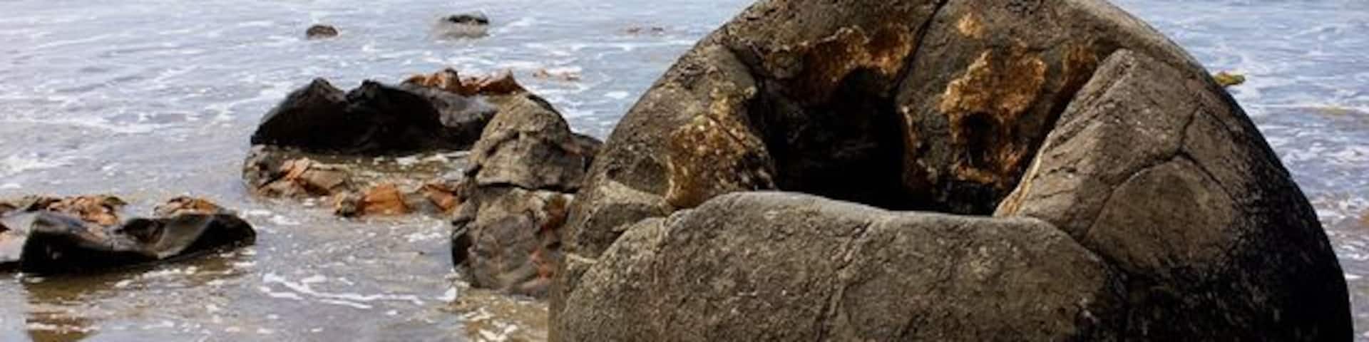 A large rock formation on a beach with the ocean in the background.
