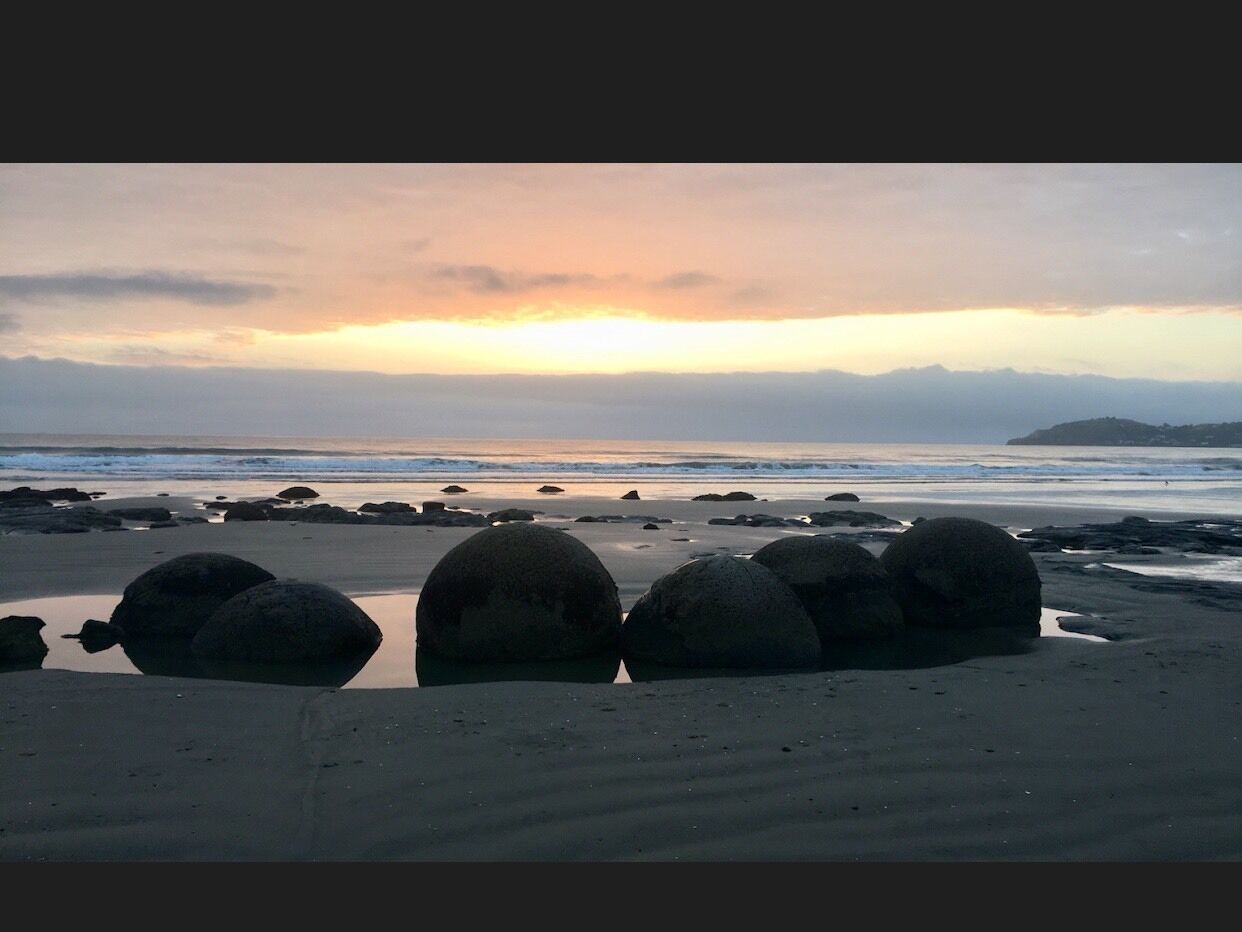A beach with large boulders and a sunset over the ocean.