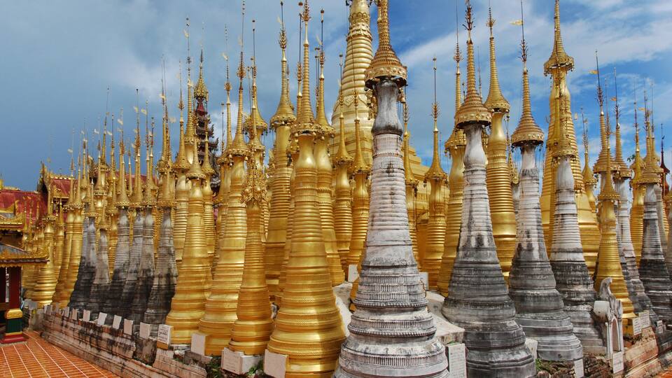 A temple with numerous golden spires and a smaller building with a red roof.