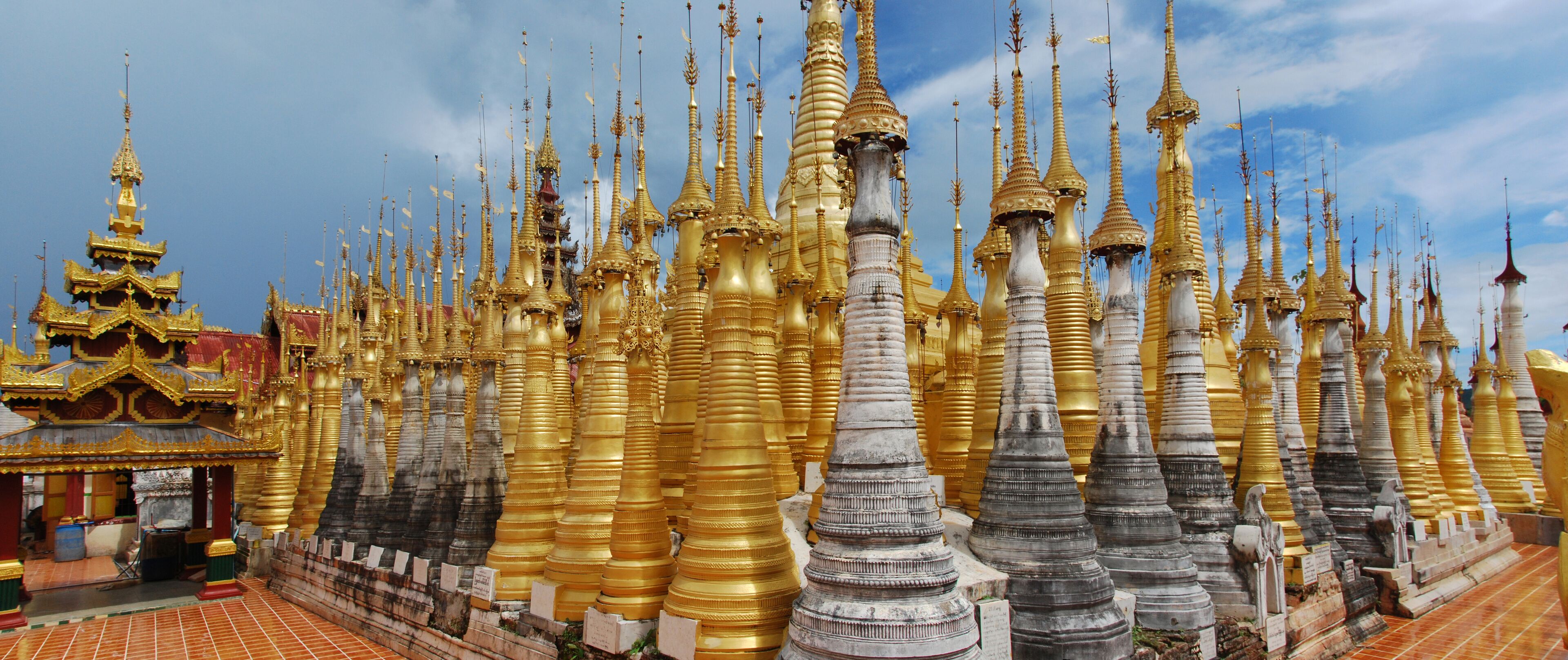 A temple with numerous golden spires and a smaller building with a red roof.