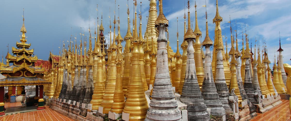 A temple with numerous golden spires and a smaller building with a red roof.