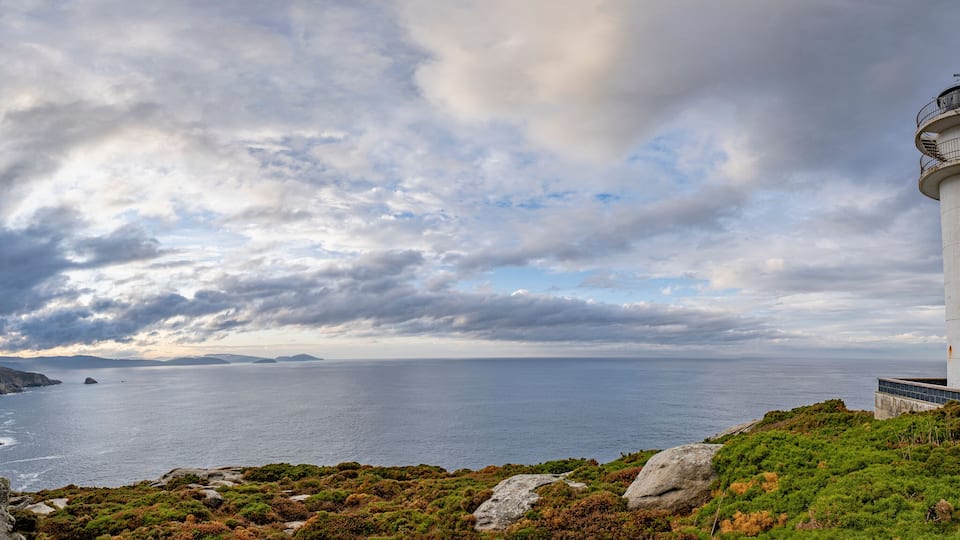 A lighthouse on a rocky coastline with a cloudy sky.