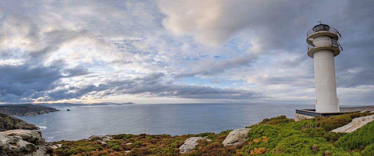 A lighthouse on a rocky coastline with a cloudy sky.
