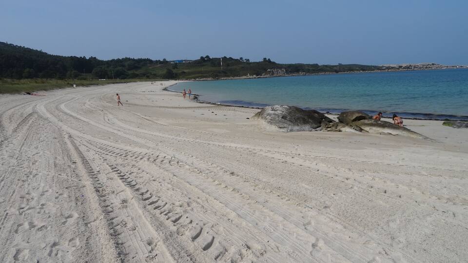 A sandy beach with footprints, a rocky outcrop, and a clear blue sky.