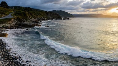 A coastal landscape with rocky shores, waves, and a winding road leading to a mountainous backdrop.