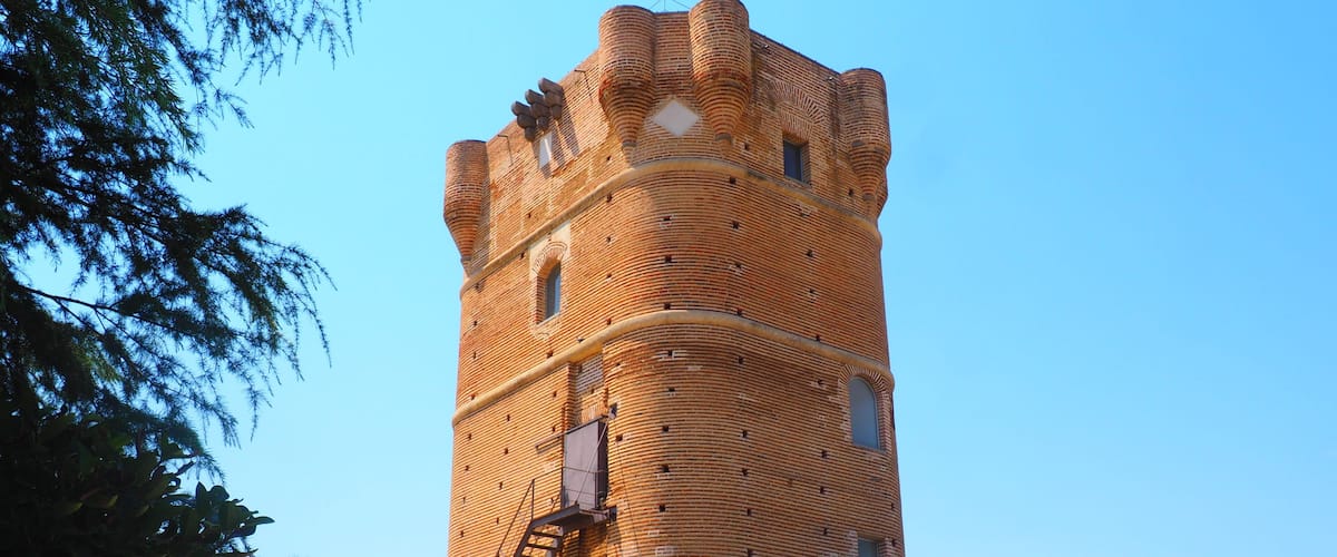 A tall brick tower with a spiral staircase and a covered viewing platform.