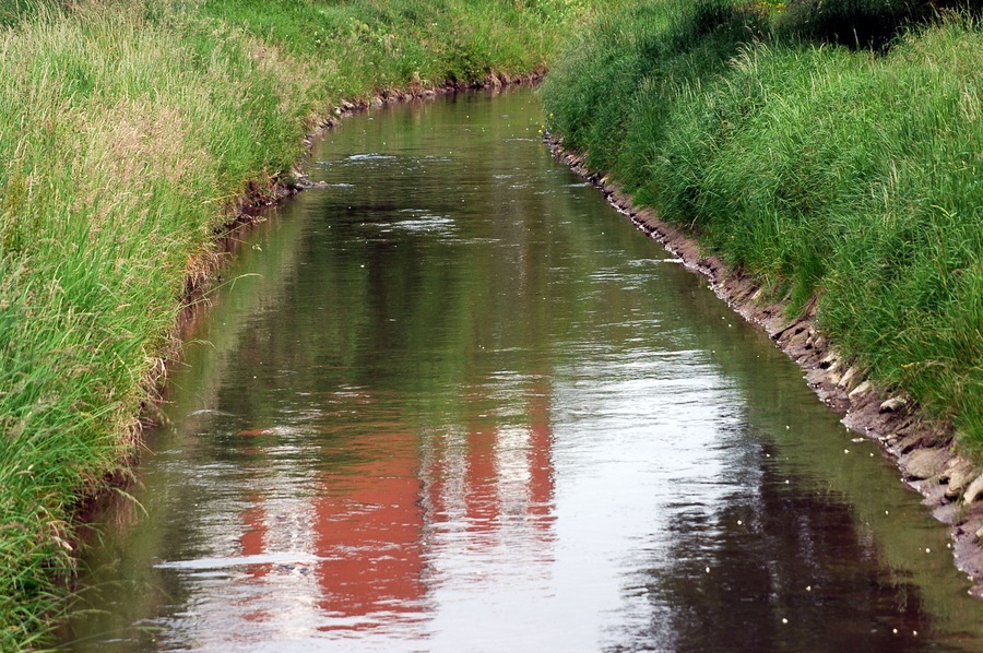 A narrow water channel bordered by green grass and a stone edge.