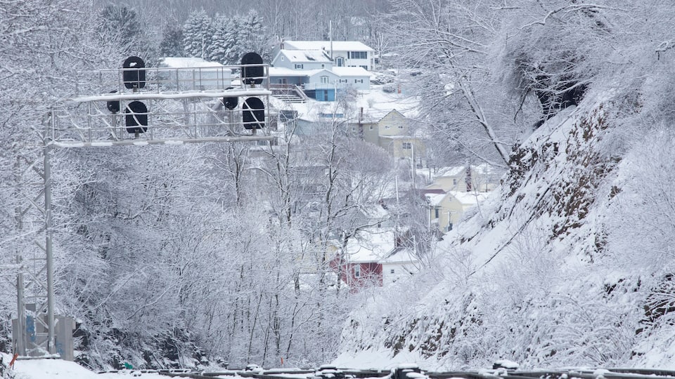 A snow-covered landscape with a railway track, a bridge, and houses in the background.