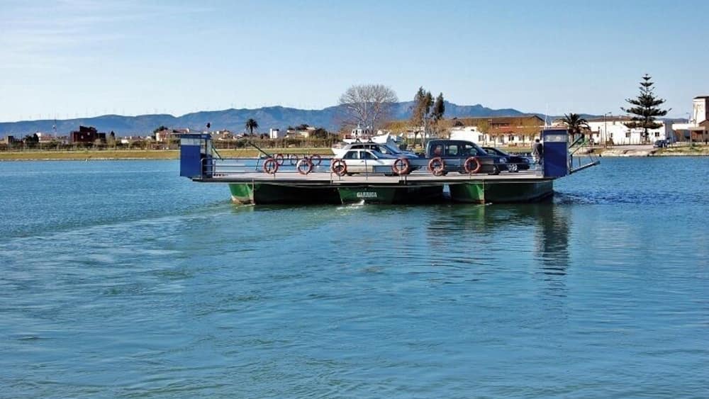 A ferry with a car and a truck on it, moving on a calm body of water.