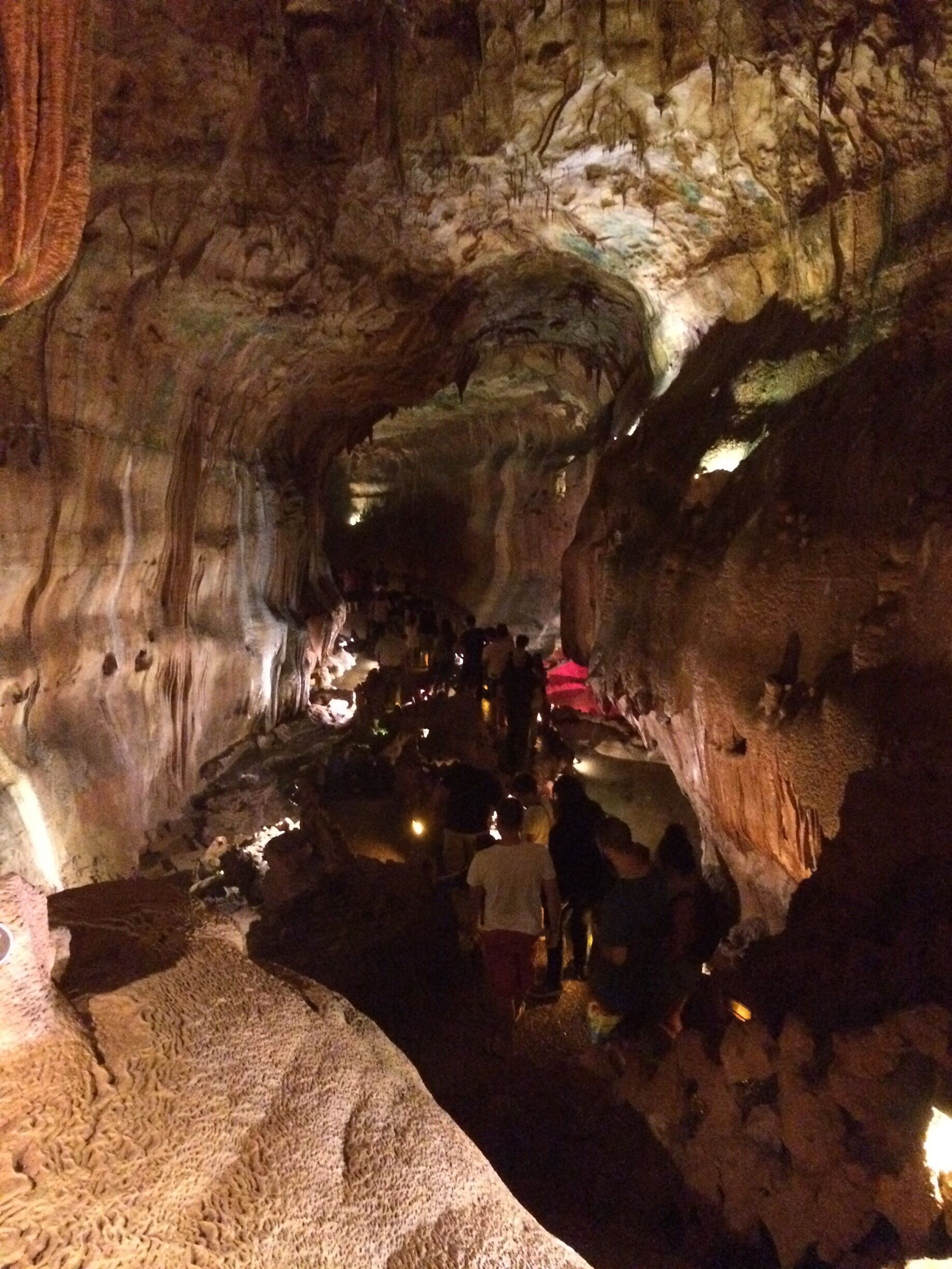 A cave with stalactites and stalagmites, illuminated by artificial lights.