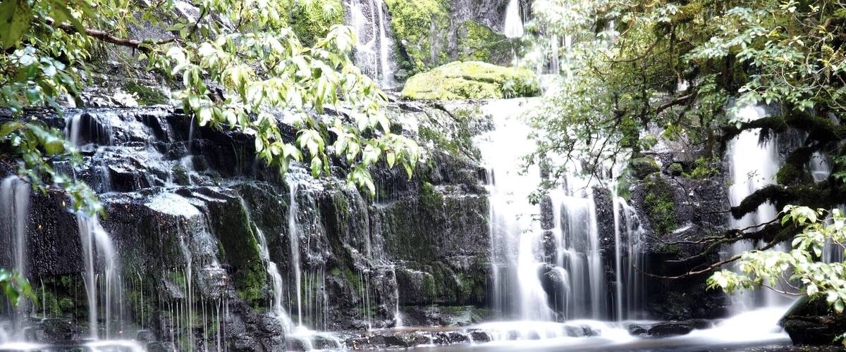 A multi-tiered waterfall cascading over rocks in a forested area.