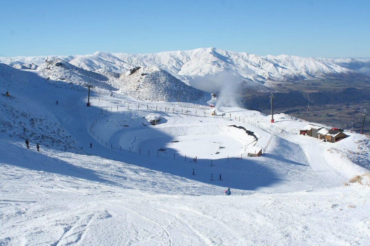 A snow-covered ski slope with a chairlift, ski tracks, and a mountain range in the background.