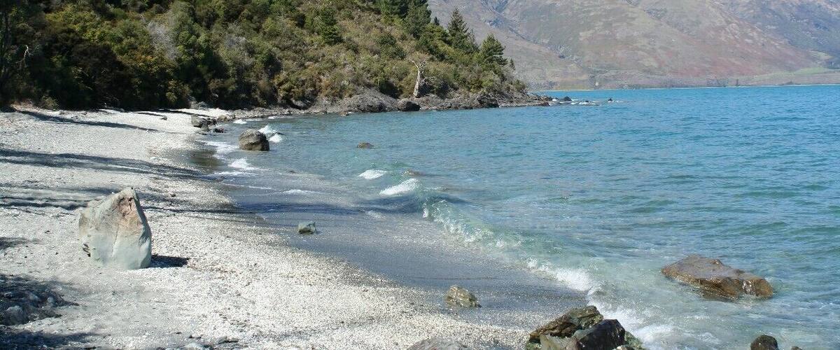 A clear lake with rocky shores, surrounded by mountains and dense forest.