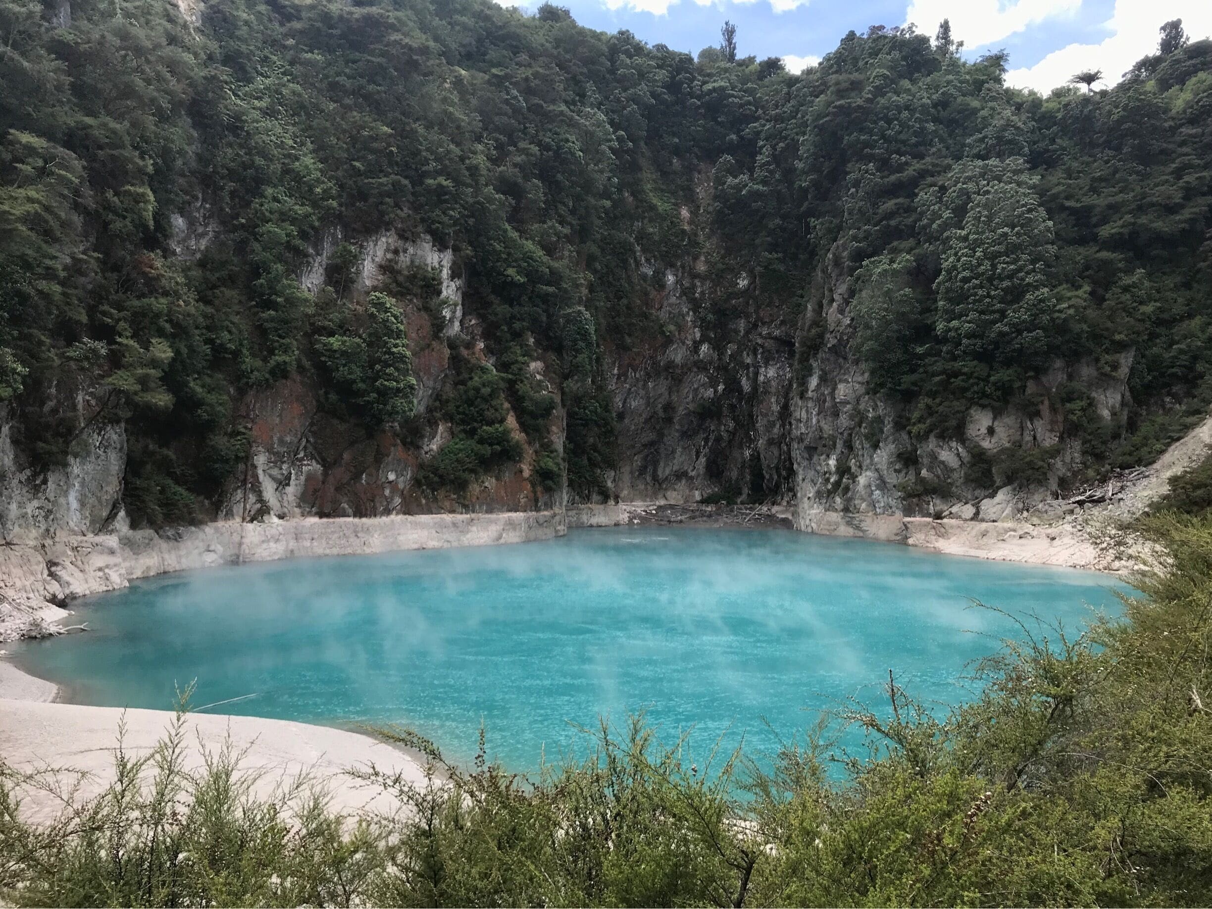 A turquoise pool surrounded by rocky cliffs and dense forest.