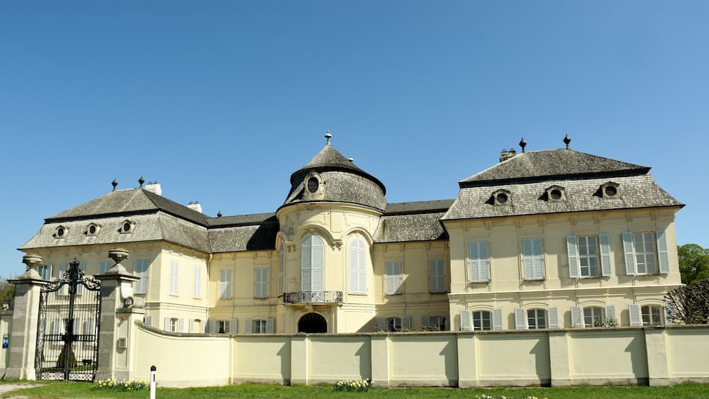 A large, historic building with a central dome, multiple chimneys, and a gated entrance.