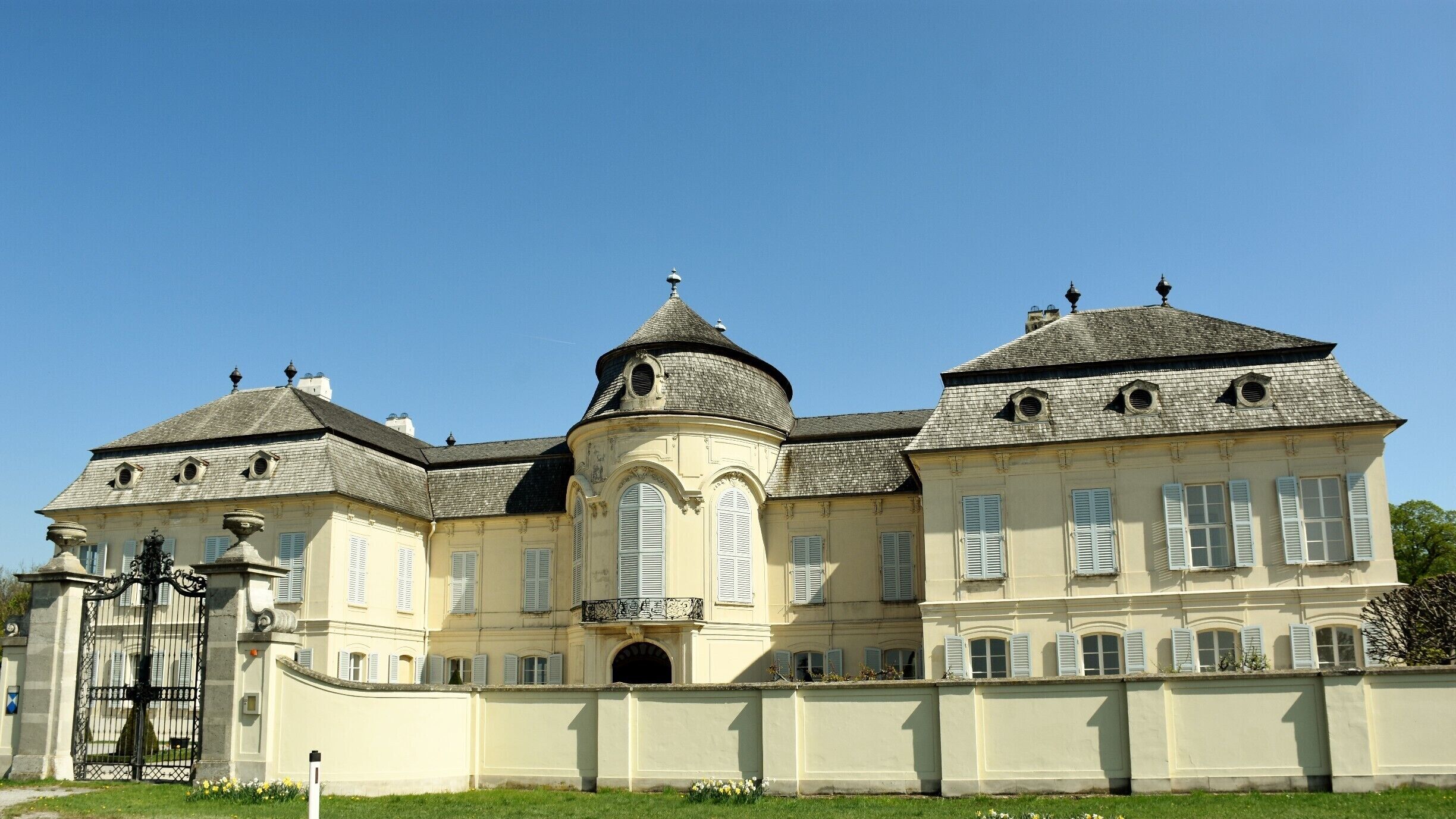 A large, historic building with a central dome, multiple chimneys, and a gated entrance.