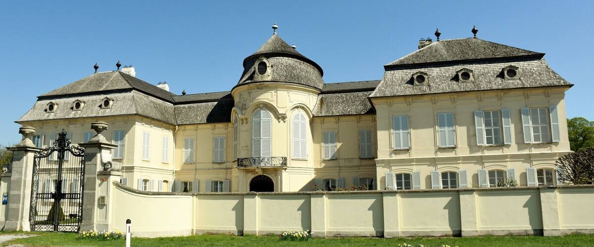 A large, historic building with a central dome, multiple chimneys, and a gated entrance.