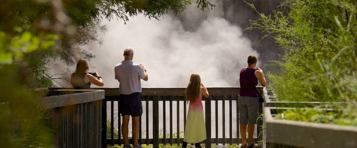 A group of people standing on a wooden deck overlooking a misty waterfall.