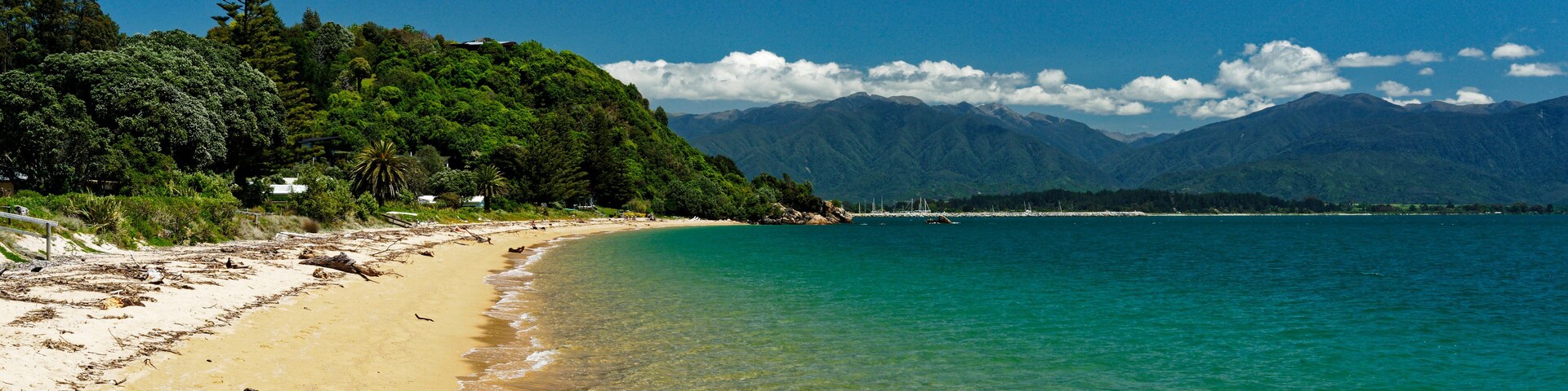 Una playa con agua turquesa cristalina, una orilla de arena y una colina boscosa al fondo.