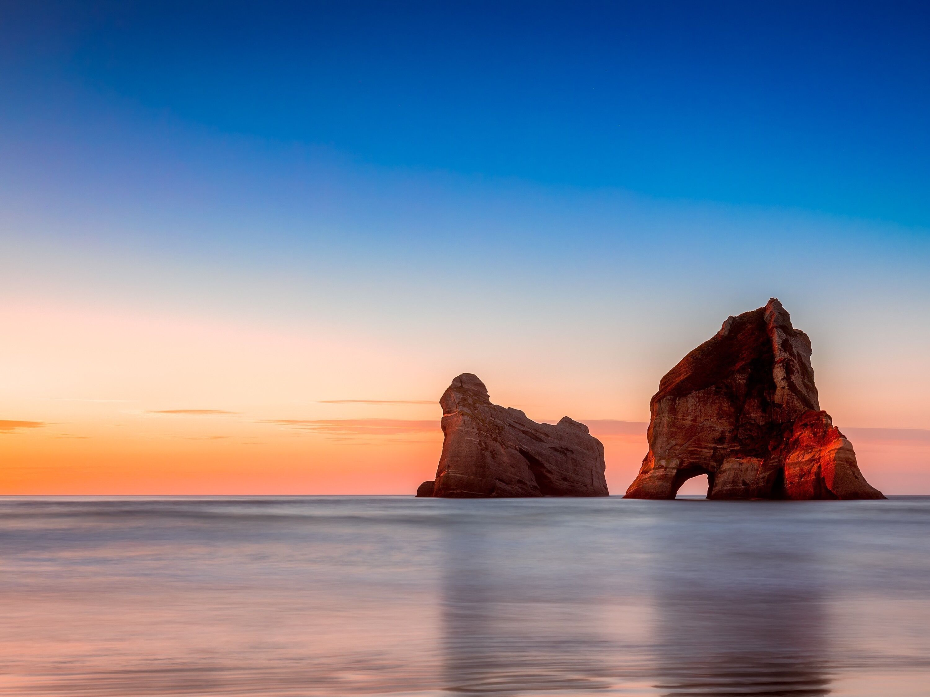 A coastal landscape with two prominent rock formations during sunset.