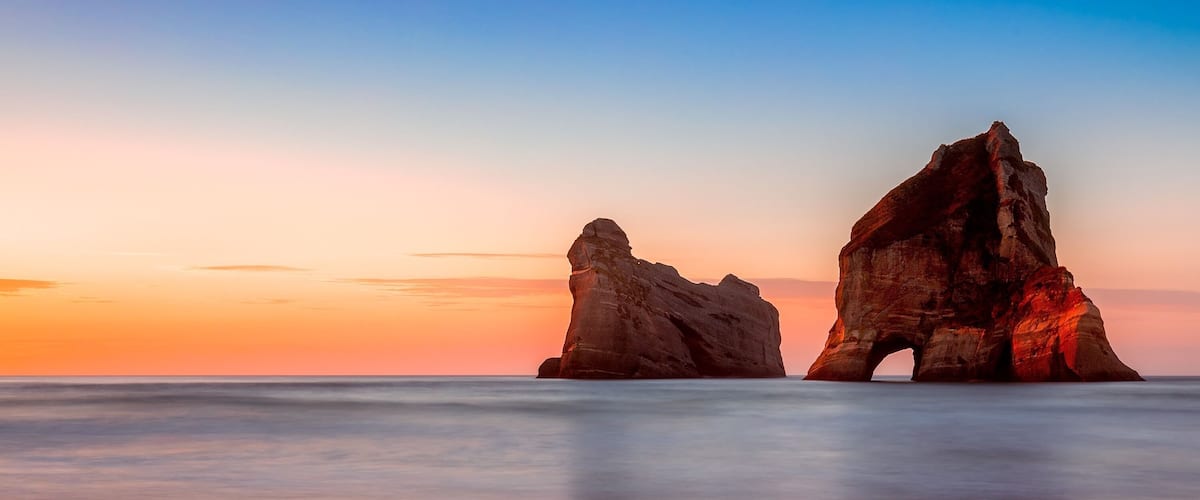 A coastal landscape with two prominent rock formations during sunset.
