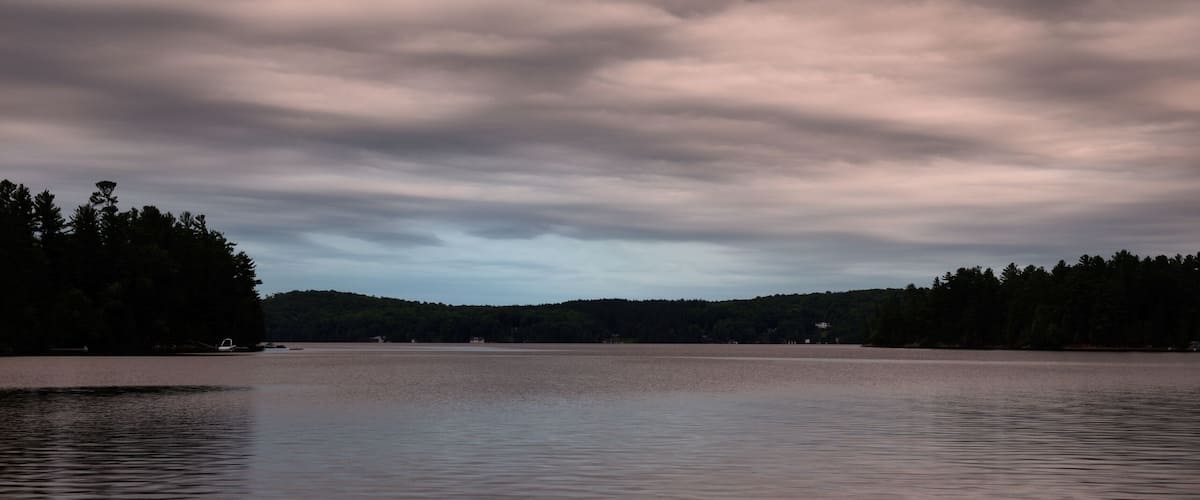 A calm lake with a forested shoreline under a cloudy sky.