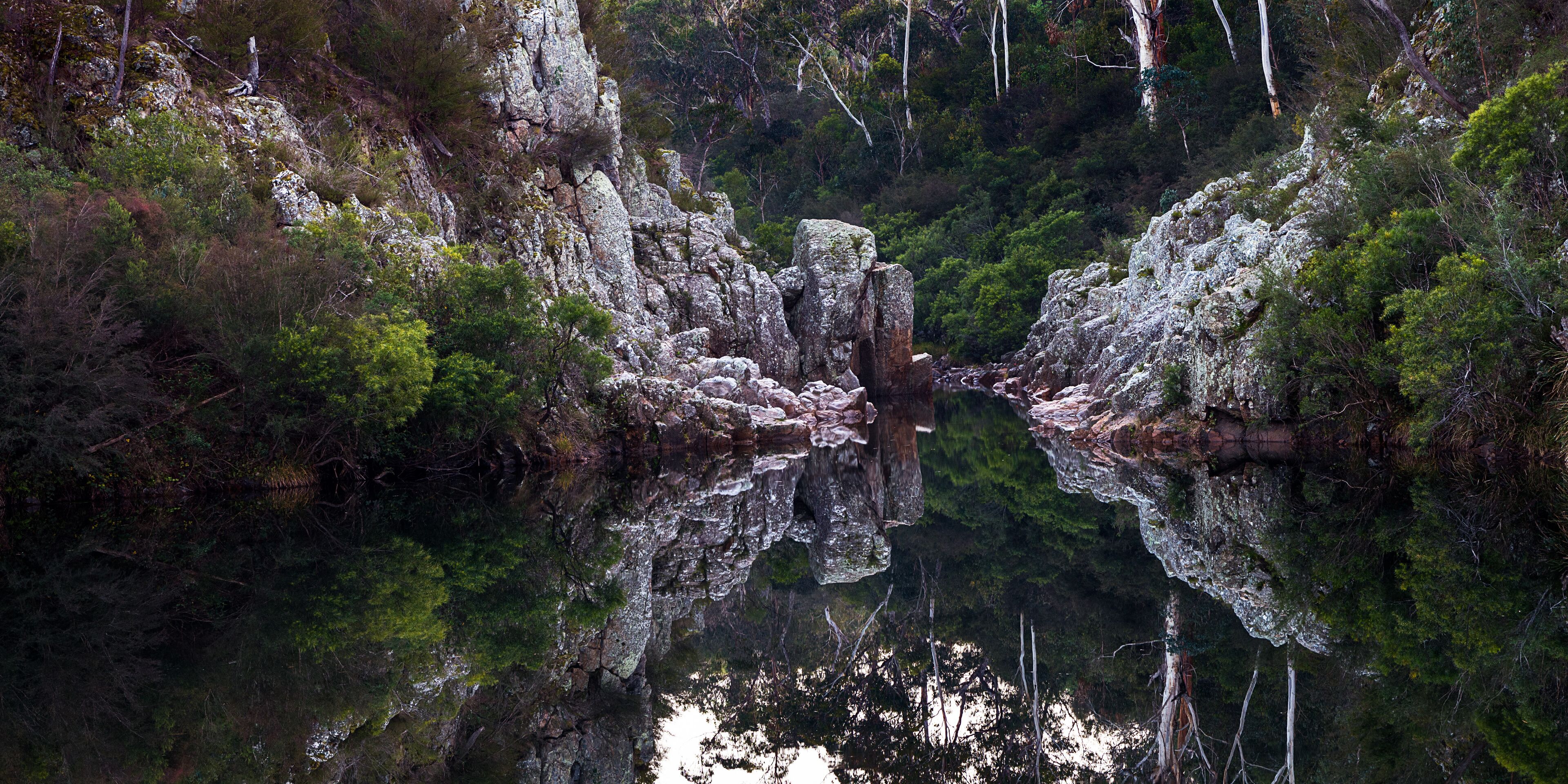 A rocky gorge with dense green foliage and a calm reflective water surface.
