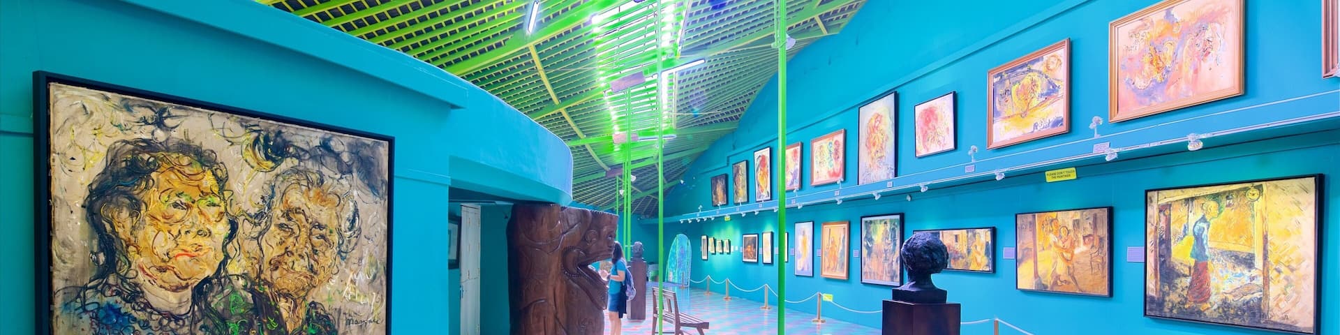 A vibrant art gallery with colorful paintings on teal walls and a checkered floor.