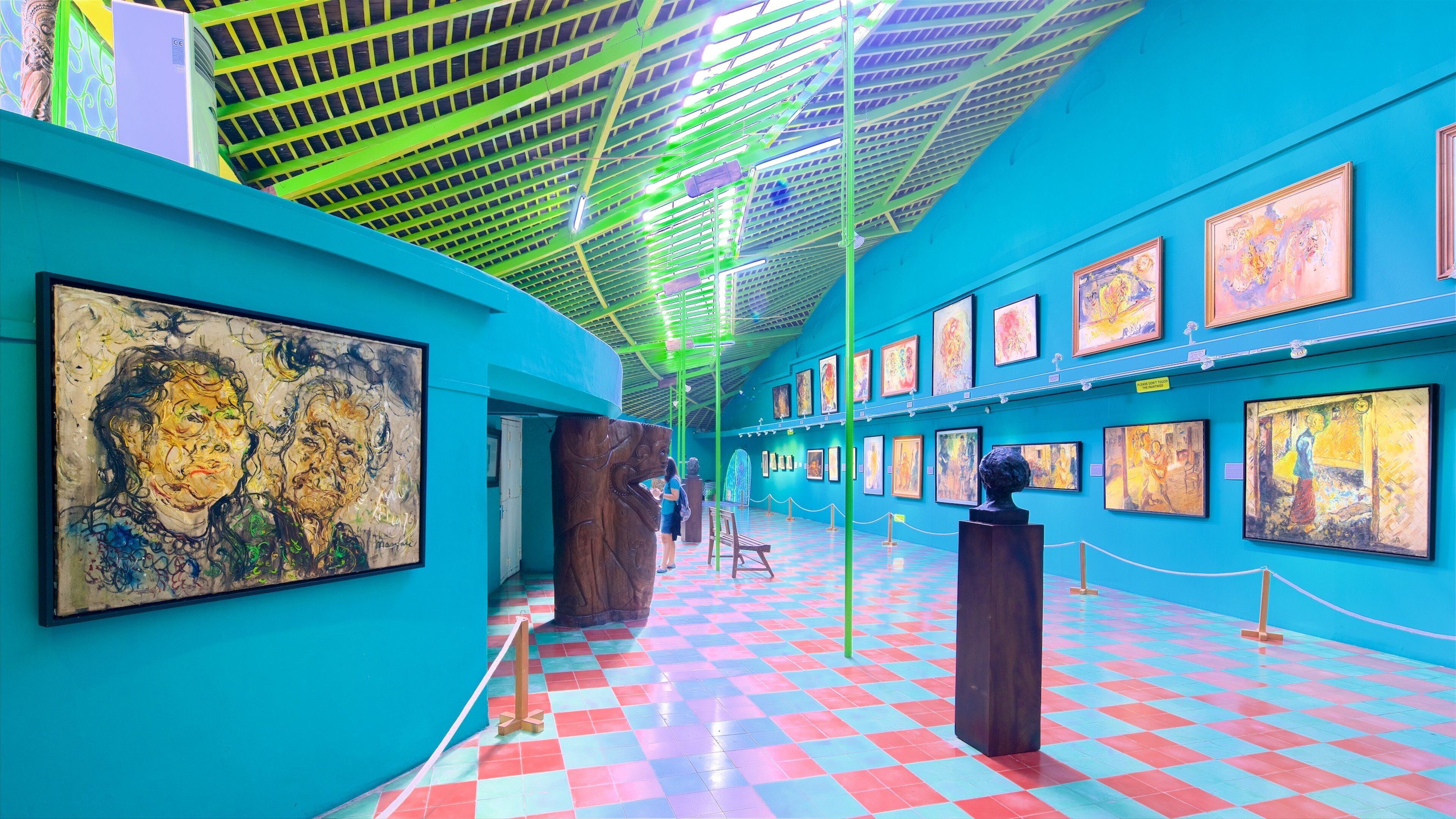 A vibrant art gallery with colorful paintings on teal walls and a checkered floor.