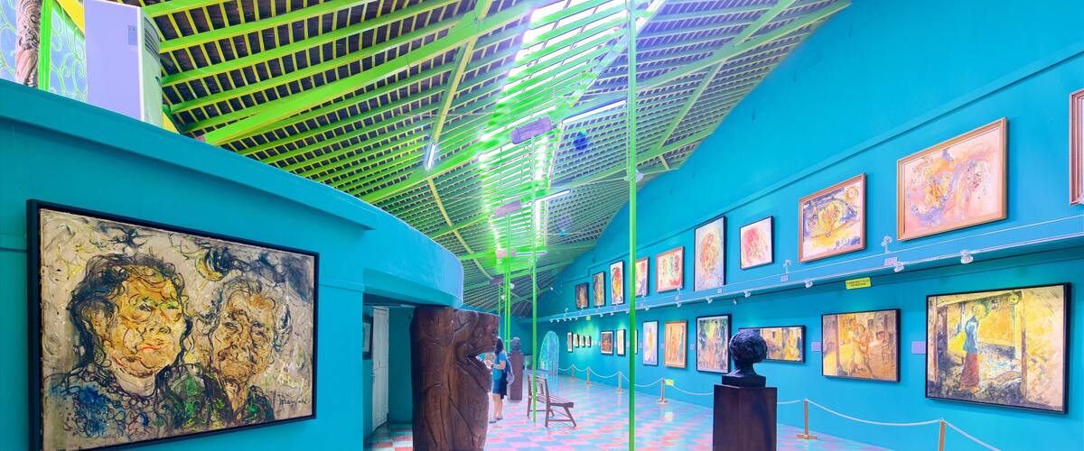 A vibrant art gallery with colorful paintings on teal walls and a checkered floor.