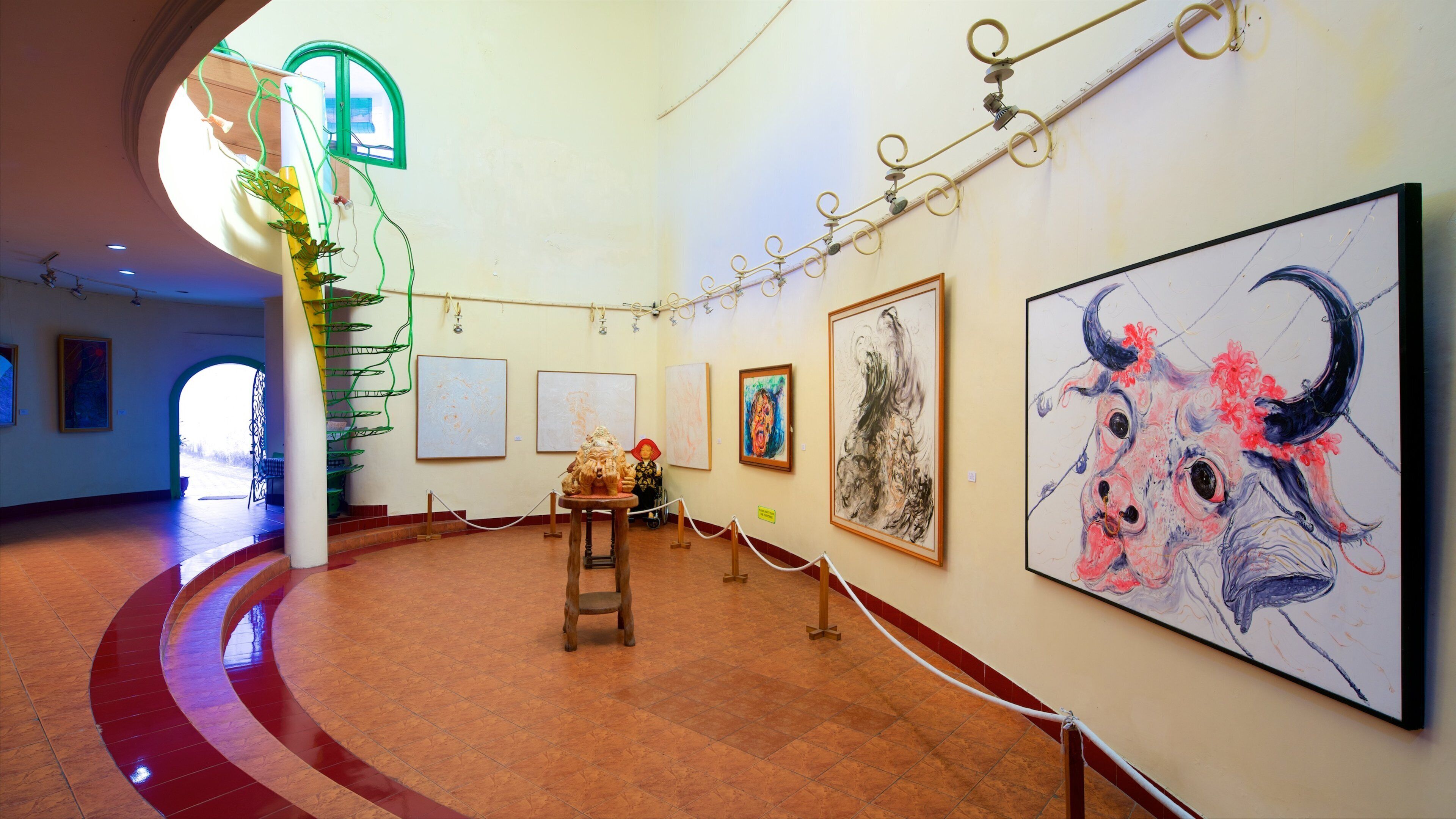 An art gallery with various paintings, a spiral staircase, and a large bull painting.