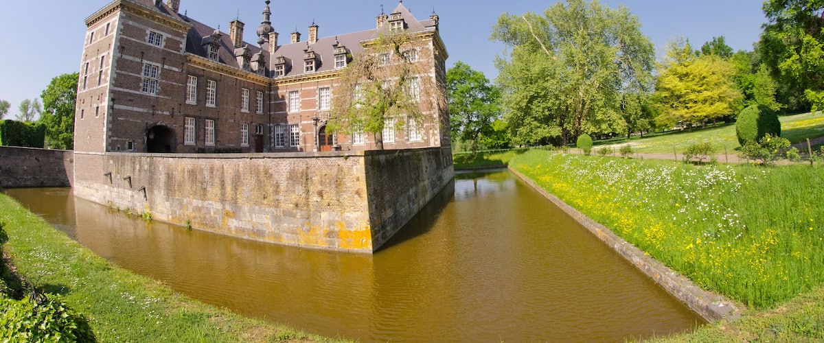 A historic building with a moat, surrounded by lush greenery and trees.