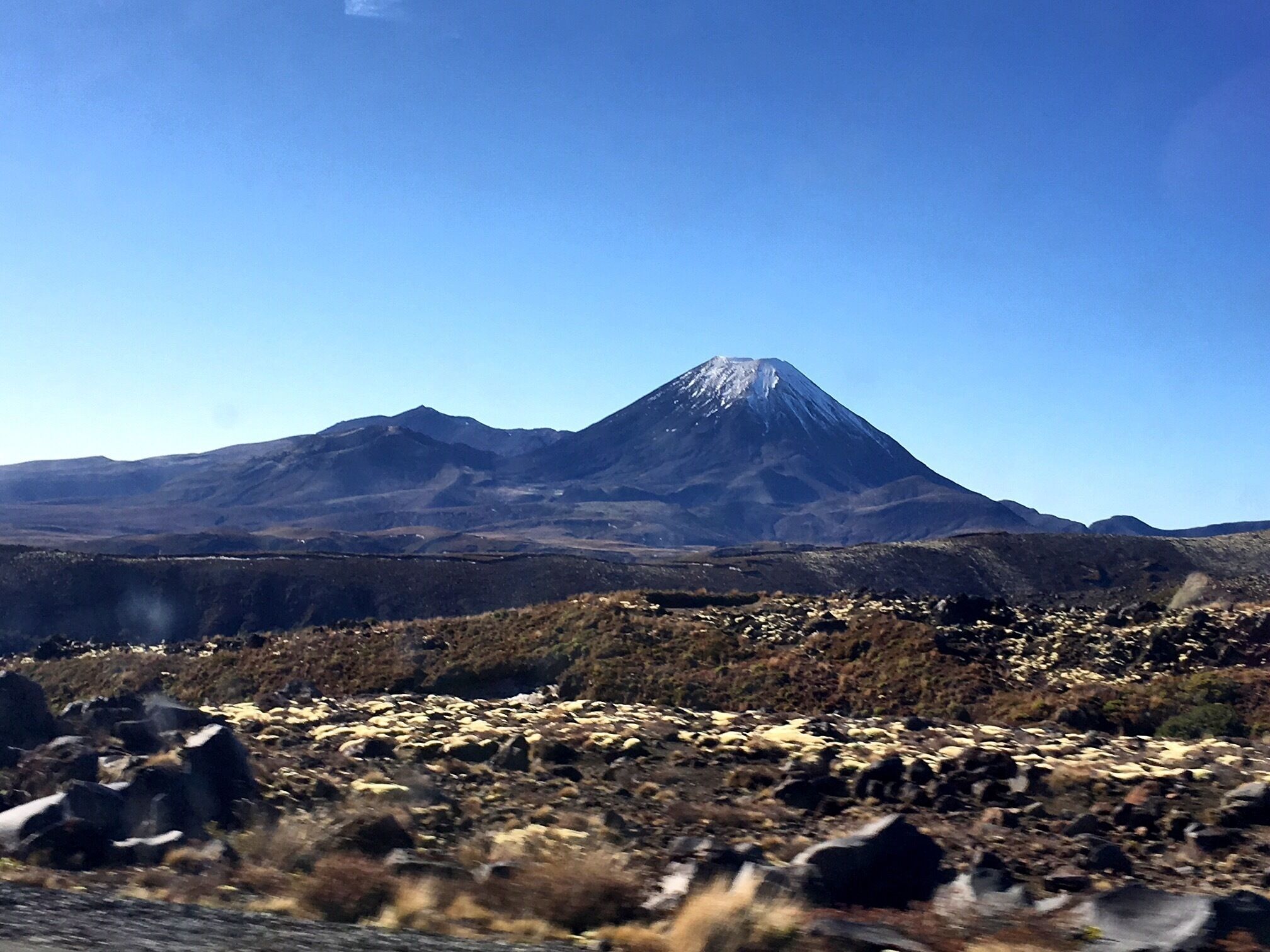 A mountain with a snow-capped peak, surrounded by rocky terrain and sparse vegetation.