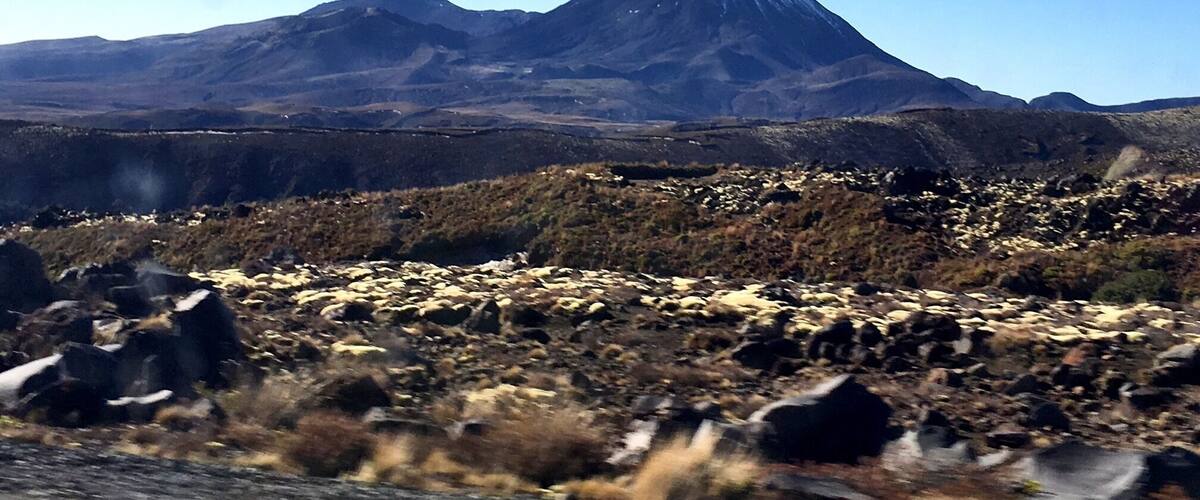 A mountain with a snow-capped peak, surrounded by rocky terrain and sparse vegetation.