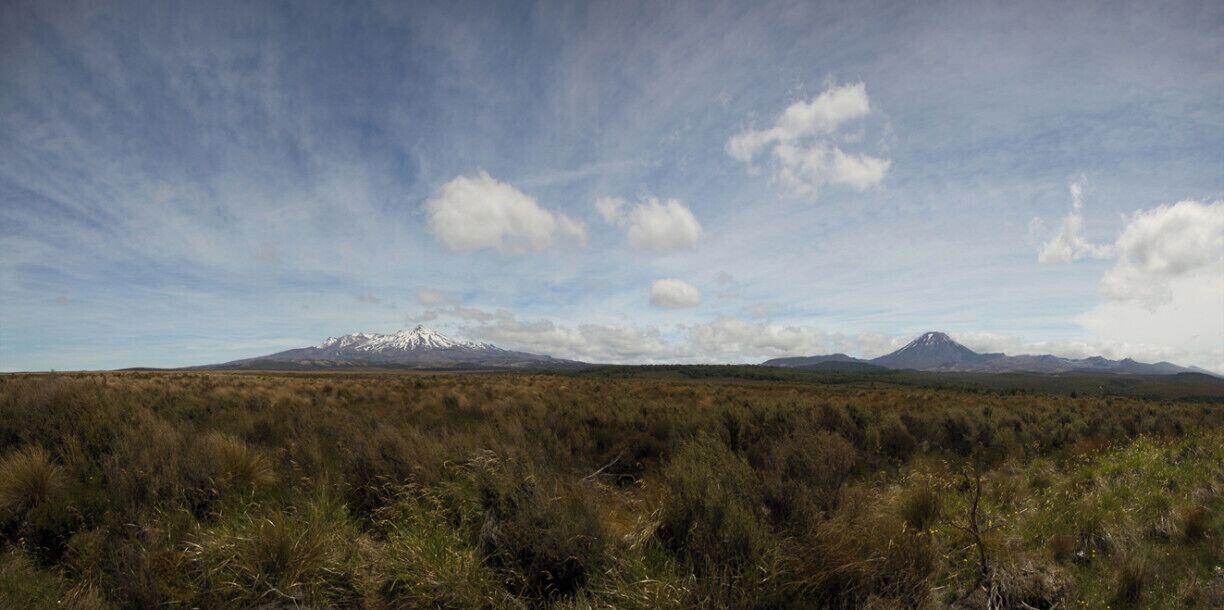 A mountainous landscape with a prominent snow-capped peak in the distance and a smaller hill in the foreground.