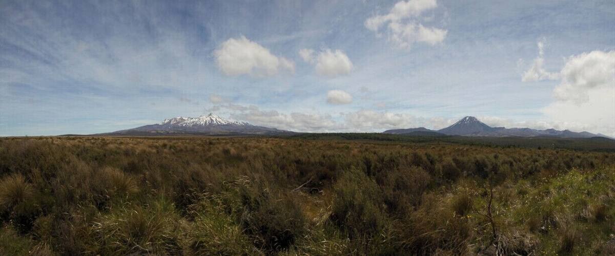 A mountainous landscape with a prominent snow-capped peak in the distance and a smaller hill in the foreground.